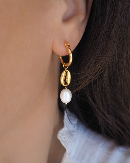 Gold cowrie shell earrings with freshwater pearls in ear model