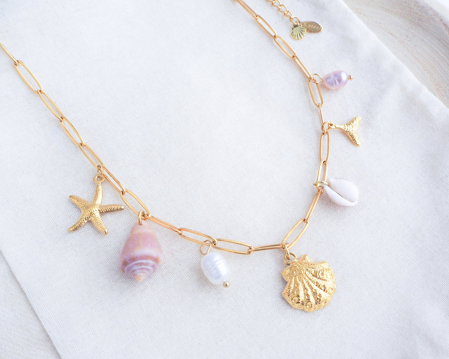 Gold Ocean Charm Necklace on display with freshwater pearls, cone shell, cowrie shell, starfish sea star and whale tail pendants. 