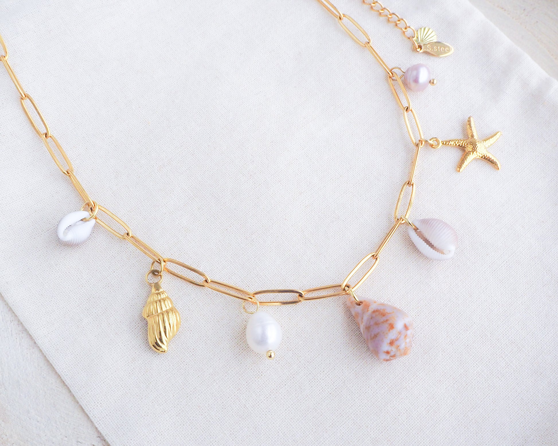 Gold Ocean Shell Charm Necklace on display tiny cone and cowrie shells, freshwater pearls, starfish sea star and whale tail pendants. 