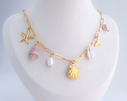 Gold Ocean Charm Necklace on neck with freshwater pearls, cone shell, cowrie shell, starfish sea star and whale tail pendants. 