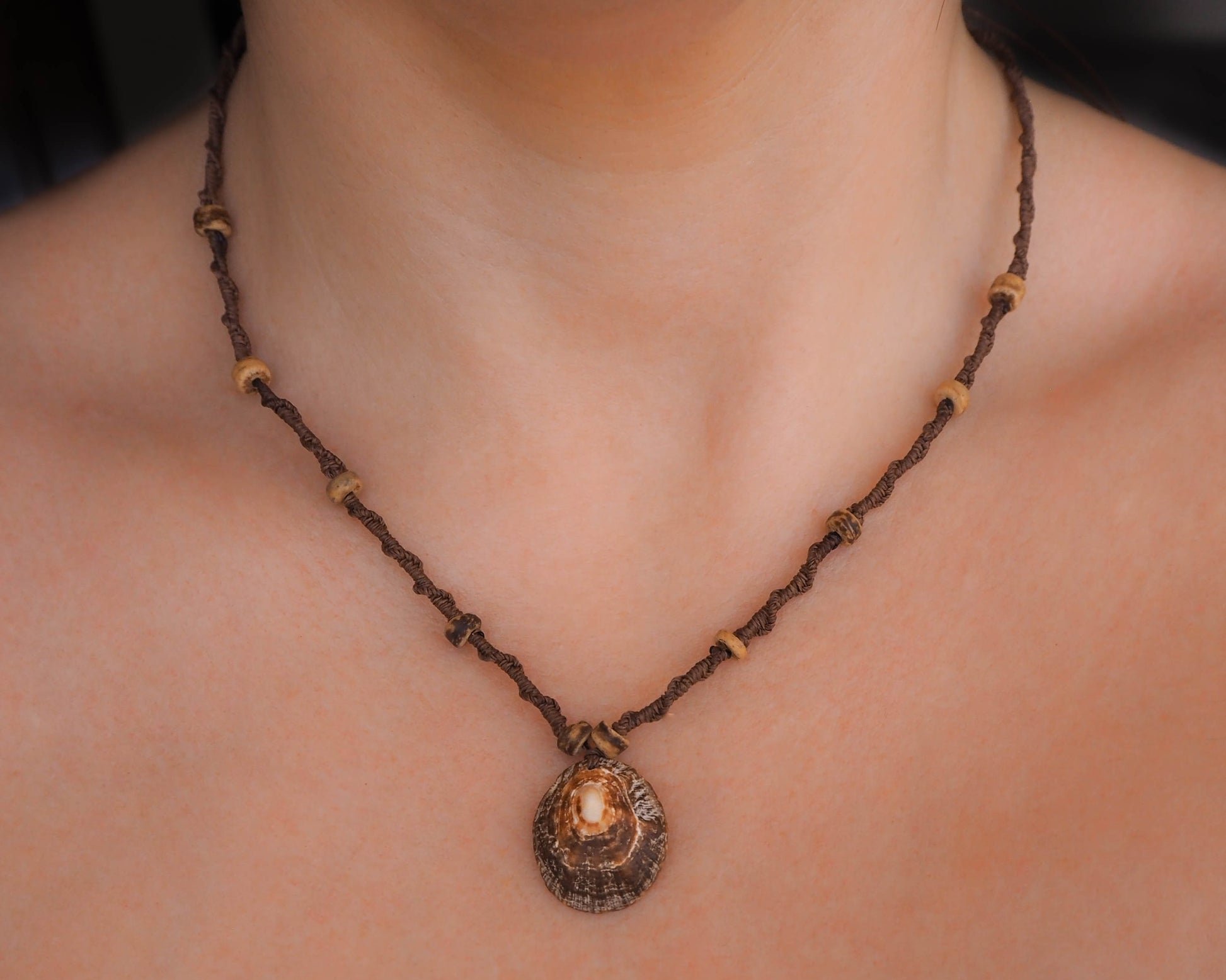 A lifestyle shot of the necklace being worn. It gracefully rests against the wearer's collarbone, the limpet shell pendant catching the light with its iridescent hues. The wooden beads add a natural and earthy touch to the ensemble.