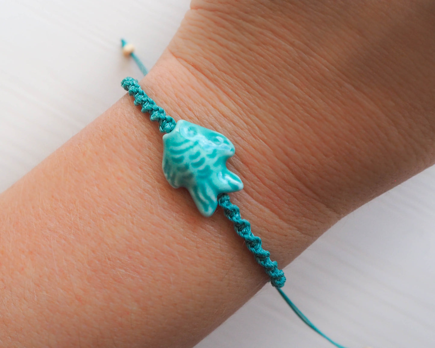 A photo displaying the entire Fish Bracelet, elegantly worn on a wrist. The bracelet adds a touch of marine-inspired sophistication to the outfit, Seabylou, Ceramic Fish bracelet, Turquoise green ocean bracelet, braided bracelet