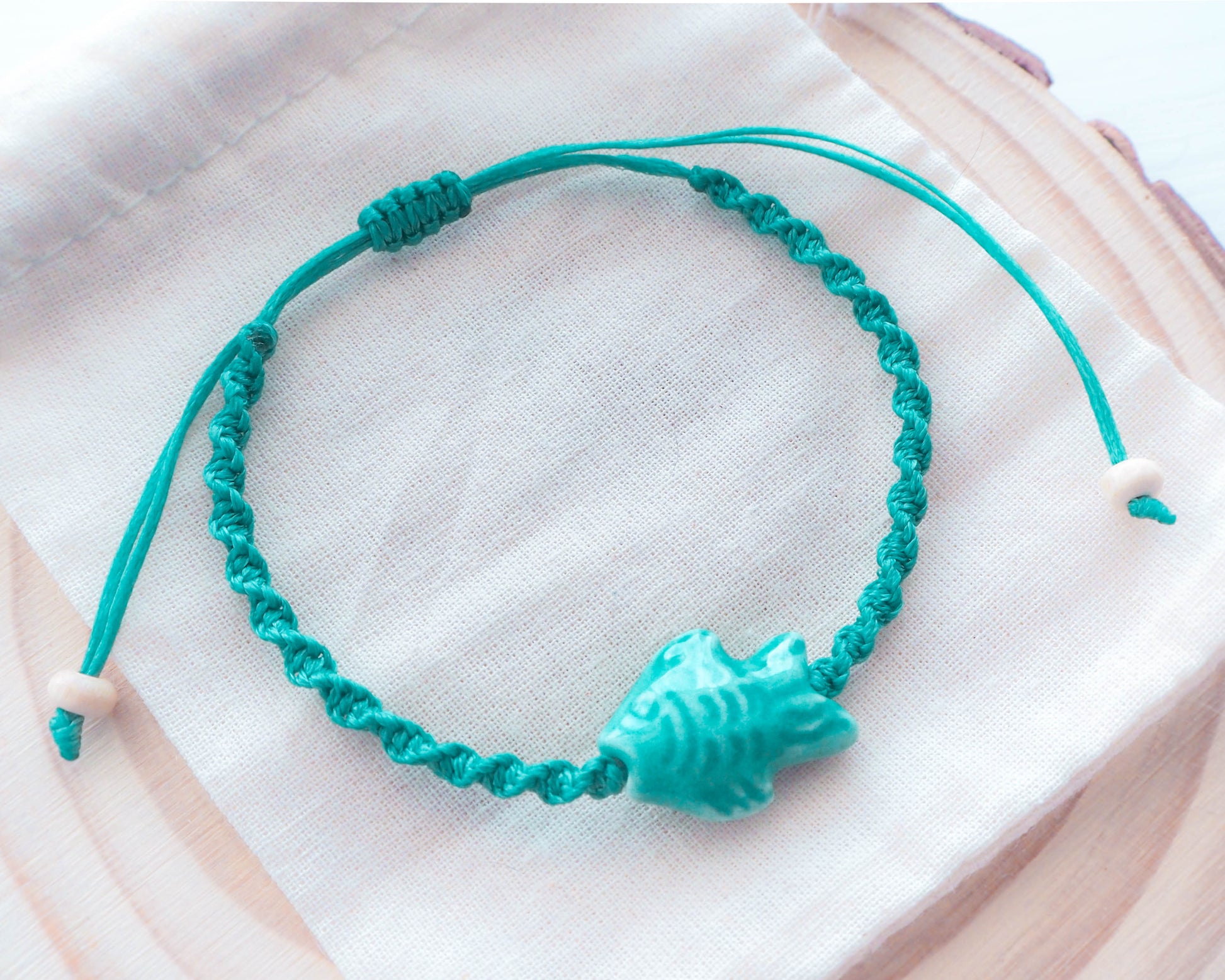 A close-up photo of the Fish Bracelet's intricate ceramic fish charm with shimmering green enamel detailing, Ceramic fish bead, green turquoise braided braccelet