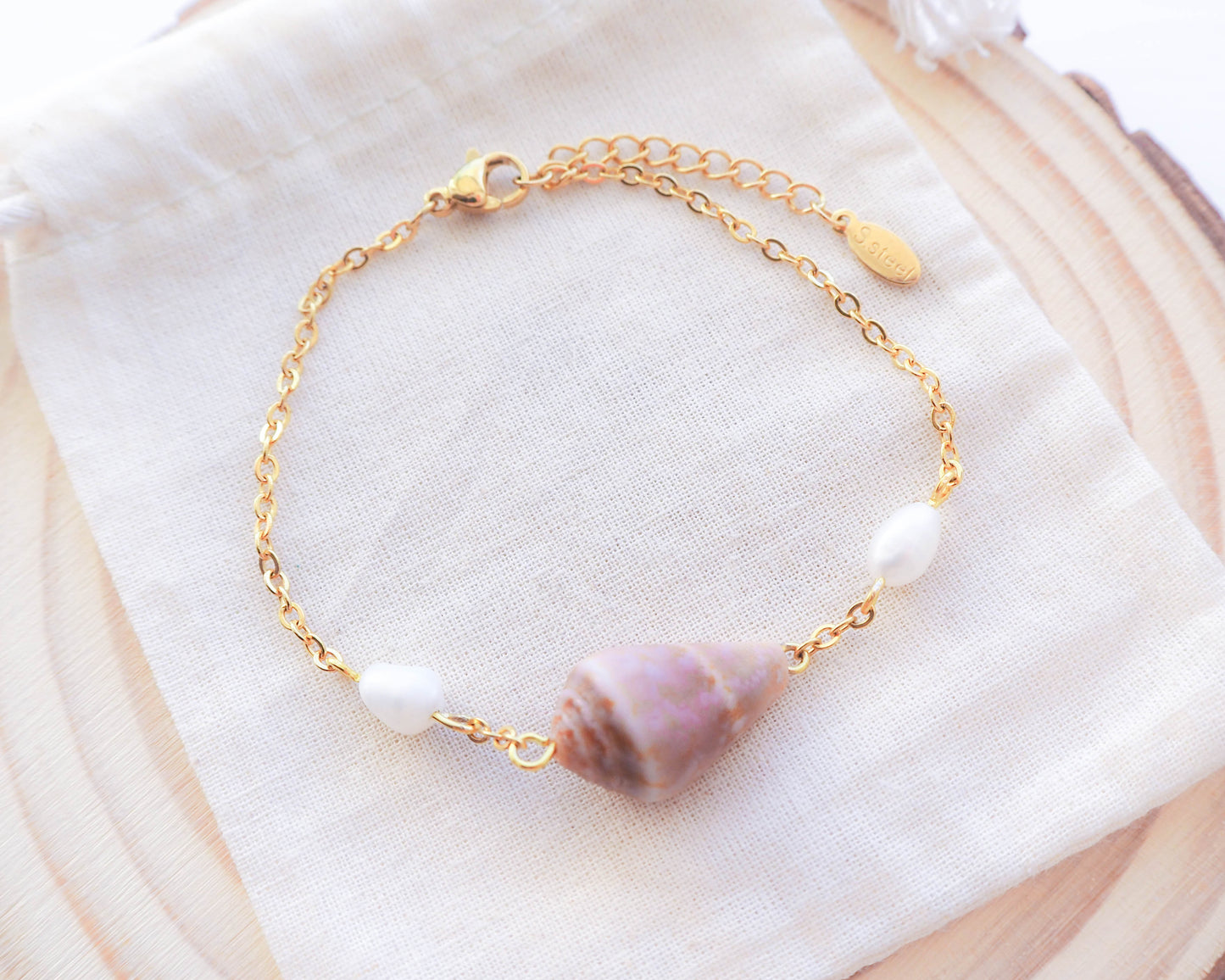 Seaside Sophistication: Close-up of Gold Cone Shell and Freshwater Pearl Bracelet on Gold Chain