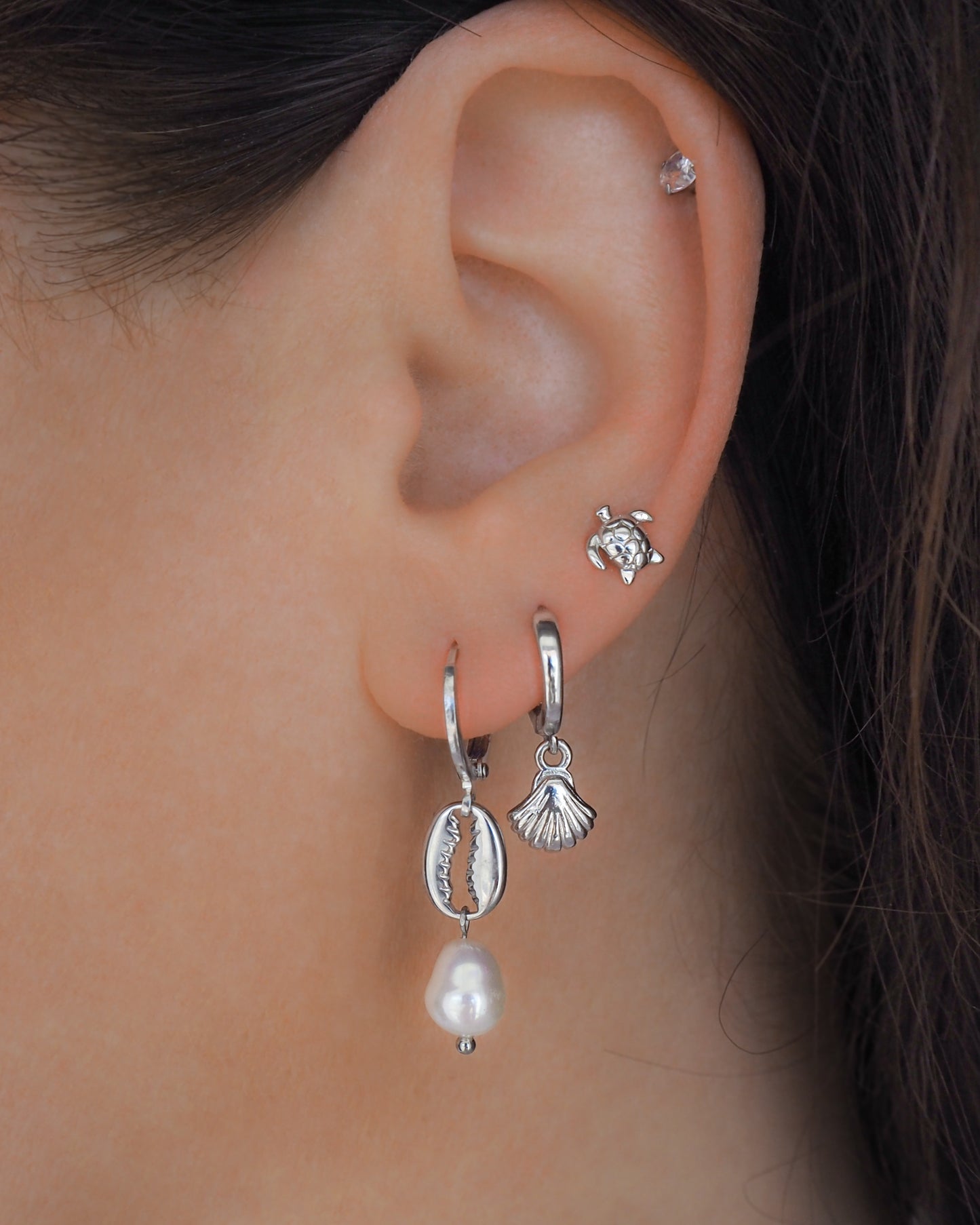 Model wearing silver cowrie shell earrings paired with a natural pearl